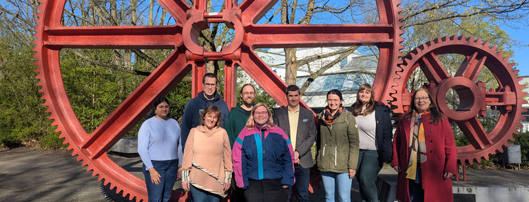 The members of the Technical Biology 2025 working group in front of the giant red cogwheels at TU Dortmund University